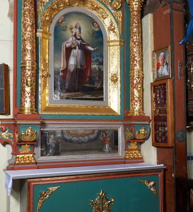 Zdjęcie nr 2: Ołtarz architektoniczny, jednokondygnacyjny. Mensa drewniana na murowanej prostopadłościennej skrzyni. Antepedium w kształcie prostokąta, w profilowanej ramie, z płaskorzeźbionymi splecionymi literami imienia Maria pośrodku i dwiema uskrzydlonymi główkami aniołków w górnych narożach. Retabulum z wydzieloną predellą ujętą po bokach konsolkami, flankowane parą kolumn. Kolumny o kapitelach korynckich i trzonach dekorowanych wicią roślinną, w jednej trzeciej wysokości przedzielone opaską. Kolumny wspierają wyłamane belkowanie zwieńczone profilowanym gzymsem. W polu środkowym prostokątna nisza zamknięta łukiem półkolistym, ujęta szeroką, złoconą ramą zdobioną uskrzydlonymi główkami aniołków. W polu niszy obraz z przedstawieniem św. Wojciecha. Predella dekorowana płyciną z malowaną sceną z przedstawieniem Zwiastowania NMP. Konsole kolumn i flankujące nastawę dekorowane na krawędziach wolutowo skręconą wicią roślinną. Belkowanie zdobione rozetami, w partii fryzu pośrodku aplikowana rzeźbiona uskrzydlona główka anielska. Całość struktury polichromowana w dwóch odcieniach: jasnobłękitnym oraz brązowym, detal architektoniczny i profilowania złocone i srebrzone.