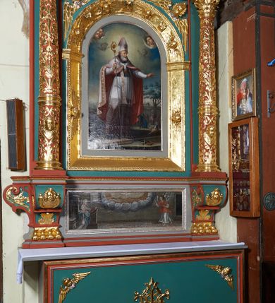 Zdjęcie nr 3: Ołtarz architektoniczny, jednokondygnacyjny. Mensa drewniana na murowanej prostopadłościennej skrzyni. Antepedium w kształcie prostokąta, w profilowanej ramie, z płaskorzeźbionymi splecionymi literami imienia Maria pośrodku i dwiema uskrzydlonymi główkami aniołków w górnych narożach. Retabulum z wydzieloną predellą ujętą po bokach konsolkami, flankowane parą kolumn. Kolumny o kapitelach korynckich i trzonach dekorowanych wicią roślinną, w jednej trzeciej wysokości przedzielone opaską. Kolumny wspierają wyłamane belkowanie zwieńczone profilowanym gzymsem. W polu środkowym prostokątna nisza zamknięta łukiem półkolistym, ujęta szeroką, złoconą ramą zdobioną uskrzydlonymi główkami aniołków. W polu niszy obraz z przedstawieniem św. Wojciecha. Predella dekorowana płyciną z malowaną sceną z przedstawieniem Zwiastowania NMP. Konsole kolumn i flankujące nastawę dekorowane na krawędziach wolutowo skręconą wicią roślinną. Belkowanie zdobione rozetami, w partii fryzu pośrodku aplikowana rzeźbiona uskrzydlona główka anielska. Całość struktury polichromowana w dwóch odcieniach: jasnobłękitnym oraz brązowym, detal architektoniczny i profilowania złocone i srebrzone.