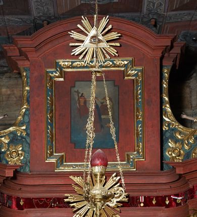 Zdjęcie nr 5:  Nastawa ołtarzowa architektoniczna, jednoosiowa, jednokondygnacyjna, na cokole, ze zwieńczeniem, z bramkami po bokach. Mensa drewniana z portatylem z marmuru dębnickiego, osadzona na murowanej, prostopadłościennej skrzyni. Antepedium w kształcie leżącego prostokąta, w profilowanej ramie z współczesnym obrazem Ostatnia Wieczerza, wzorowanym na fresku Leonarda da Vinci. Retabulum ujęte parą wklęsłych pilastrów oraz parą kolumn o kapitelach jońskich i gładkich trzonach, umieszczonych na ustawionych ukośnie cokołach. Podpory dźwigają pełne belkowanie o wklęsło-wypukłej linii, występujące ukośnie w osi kolumn. W polu środkowym profilowana rama w kształcie stojącego prostokąta. Zwieńczenie w kształcie stojącego prostokąta zamkniętego łukiem odcinkowym nadwieszonym i ujętego okazałymi spływami wolutowymi. W polu rama obrazu w formie stojącego prostokąta o wciętych narożach. Bramki z drzwiczkami, z przejściami w kształcie stojącego prostokąta zamkniętego łukiem półkolistym nadwieszonym, zwieńczone gzymsem, na którym w osi bramek cokoły ujęte spływami wolutowymi. Cokoły dekorowane płycinami z akantem w formie karbowanej wstęgi. Kolumny z dwóch stron flankują płyciny z festonami zwieńczone pasem z dekoracją geometryczną. W polu środkowym nastawy obraz Matka Boska z Dzieciątkiem otoczony wotami, w ramie dekorowanej ornamentem roślinnym, flankowany stojącymi przy kolumnach figurami aniołów. We fryzie wota, ponad polem środkowym gloria promienista ze splecionymi literami imienia MARIA. Nastawa ujęta uszami utworzonymi z motywów suchego akantu. Na belkowaniu dwie figury zwrócone do wnętrza ołtarza oraz cokoły z wazonami z płaskorzeźbionymi bukietami kwiatów. W zwieńczeniu rama dekorowana ornamentem roślinnym, w niej obraz Koronacja Marii , wyżej Oko Opatrzności w glorii. Spływy zdobione karbowaną wstęgą, akantem i kwiatami. Bramki w przyłuczach dekorowane akantem, cokół z płyciną i akantem, na nim figury św. Wojciecha i św. Stanisława. Nastawa polichromowana na czerwono, płyciny i detale architektoniczne marmoryzowane w odcieniach zieleni, ornamenty złocone.