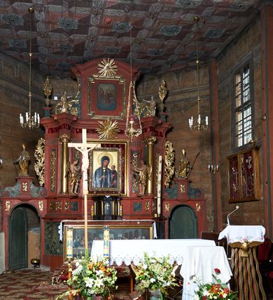 Zdjęcie nr 4:  Nastawa ołtarzowa architektoniczna, jednoosiowa, jednokondygnacyjna, na cokole, ze zwieńczeniem, z bramkami po bokach. Mensa drewniana z portatylem z marmuru dębnickiego, osadzona na murowanej, prostopadłościennej skrzyni. Antepedium w kształcie leżącego prostokąta, w profilowanej ramie z współczesnym obrazem Ostatnia Wieczerza, wzorowanym na fresku Leonarda da Vinci. Retabulum ujęte parą wklęsłych pilastrów oraz parą kolumn o kapitelach jońskich i gładkich trzonach, umieszczonych na ustawionych ukośnie cokołach. Podpory dźwigają pełne belkowanie o wklęsło-wypukłej linii, występujące ukośnie w osi kolumn. W polu środkowym profilowana rama w kształcie stojącego prostokąta. Zwieńczenie w kształcie stojącego prostokąta zamkniętego łukiem odcinkowym nadwieszonym i ujętego okazałymi spływami wolutowymi. W polu rama obrazu w formie stojącego prostokąta o wciętych narożach. Bramki z drzwiczkami, z przejściami w kształcie stojącego prostokąta zamkniętego łukiem półkolistym nadwieszonym, zwieńczone gzymsem, na którym w osi bramek cokoły ujęte spływami wolutowymi. Cokoły dekorowane płycinami z akantem w formie karbowanej wstęgi. Kolumny z dwóch stron flankują płyciny z festonami zwieńczone pasem z dekoracją geometryczną. W polu środkowym nastawy obraz Matka Boska z Dzieciątkiem otoczony wotami, w ramie dekorowanej ornamentem roślinnym, flankowany stojącymi przy kolumnach figurami aniołów. We fryzie wota, ponad polem środkowym gloria promienista ze splecionymi literami imienia MARIA. Nastawa ujęta uszami utworzonymi z motywów suchego akantu. Na belkowaniu dwie figury zwrócone do wnętrza ołtarza oraz cokoły z wazonami z płaskorzeźbionymi bukietami kwiatów. W zwieńczeniu rama dekorowana ornamentem roślinnym, w niej obraz Koronacja Marii , wyżej Oko Opatrzności w glorii. Spływy zdobione karbowaną wstęgą, akantem i kwiatami. Bramki w przyłuczach dekorowane akantem, cokół z płyciną i akantem, na nim figury św. Wojciecha i św. Stanisława. Nastawa polichromowana na czerwono, płyciny i detale architektoniczne marmoryzowane w odcieniach zieleni, ornamenty złocone.