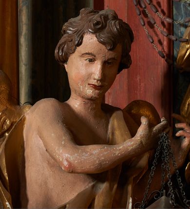 Zdjęcie nr 5: Rzeźby pełnoplastyczne, z tyłu drążone. Figury całopostaciowe, zwrócone antytetycznie, stojące w kontrapoście, z pochylonymi głowami, z obiema rękoma skierowanymi ku środkowi ołtarza, przytrzymują latarnie. Twarze owalne, o indywidualnych rysach, delikatnie zarysowanych oczach i ustach oraz płaskim nosie. Włosy w postaci krótkich, gęstych loków. Ubrane w przewiązaną diagonalnie przez tors, obficie drapowaną szatę, opadającą na tył postaci. Skrzydła złożone. Polichromia naturalistyczna w partiach ciała, szaty i skrzydła złocone.