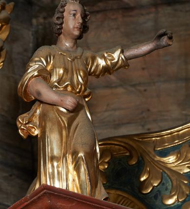 Zdjęcie nr 11: Rzeźby pełnoplastyczne, z tyłu drążone. Figury całopostaciowe, zwrócone antytetycznie, stojące w kontrapoście, z pochylonymi głowami, z obiema rękoma skierowanymi ku środkowi ołtarza, przytrzymują latarnie. Twarze owalne, o indywidualnych rysach, delikatnie zarysowanych oczach i ustach oraz płaskim nosie. Włosy w postaci krótkich, gęstych loków. Ubrane w przewiązaną diagonalnie przez tors, obficie drapowaną szatę, opadającą na tył postaci. Skrzydła złożone. Polichromia naturalistyczna w partiach ciała, szaty i skrzydła złocone.