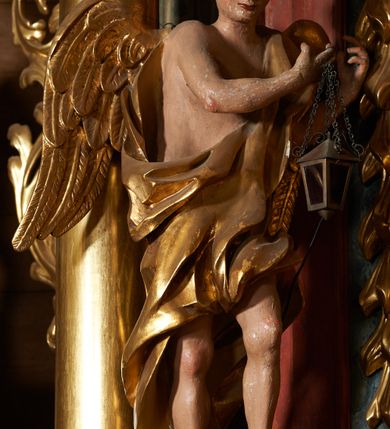 Zdjęcie nr 2: Rzeźby pełnoplastyczne, z tyłu drążone. Figury całopostaciowe, zwrócone antytetycznie, stojące w kontrapoście, z pochylonymi głowami, z obiema rękoma skierowanymi ku środkowi ołtarza, przytrzymują latarnie. Twarze owalne, o indywidualnych rysach, delikatnie zarysowanych oczach i ustach oraz płaskim nosie. Włosy w postaci krótkich, gęstych loków. Ubrane w przewiązaną diagonalnie przez tors, obficie drapowaną szatę, opadającą na tył postaci. Skrzydła złożone. Polichromia naturalistyczna w partiach ciała, szaty i skrzydła złocone.