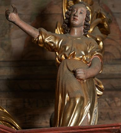 Zdjęcie nr 3: Rzeźby pełnoplastyczne, z tyłu drążone. Figury całopostaciowe, zwrócone antytetycznie, stojące w kontrapoście, z pochylonymi głowami, z obiema rękoma skierowanymi ku środkowi ołtarza, przytrzymują latarnie. Twarze owalne, o indywidualnych rysach, delikatnie zarysowanych oczach i ustach oraz płaskim nosie. Włosy w postaci krótkich, gęstych loków. Ubrane w przewiązaną diagonalnie przez tors, obficie drapowaną szatę, opadającą na tył postaci. Skrzydła złożone. Polichromia naturalistyczna w partiach ciała, szaty i skrzydła złocone.