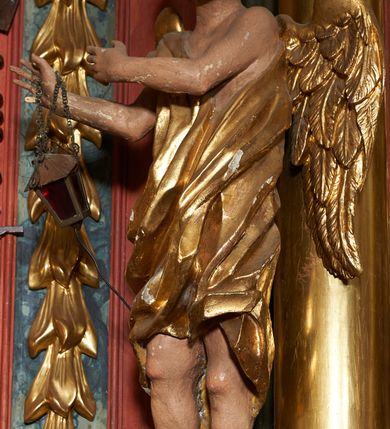 Zdjęcie nr 6: Rzeźby pełnoplastyczne, z tyłu drążone. Figury całopostaciowe, zwrócone antytetycznie, stojące w kontrapoście, z pochylonymi głowami, z obiema rękoma skierowanymi ku środkowi ołtarza, przytrzymują latarnie. Twarze owalne, o indywidualnych rysach, delikatnie zarysowanych oczach i ustach oraz płaskim nosie. Włosy w postaci krótkich, gęstych loków. Ubrane w przewiązaną diagonalnie przez tors, obficie drapowaną szatę, opadającą na tył postaci. Skrzydła złożone. Polichromia naturalistyczna w partiach ciała, szaty i skrzydła złocone.
