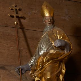 Zdjęcie nr 1: Rzeźba pełnoplastyczna, z tyłu drążona. Figura całopostaciowa, zwrócona en trois quarts w lewo, z głową skierowana w prawo, stojąca w kontrapoście i ekspresyjnym zwrocie ciała. Prawą ręką, wysuniętą w bok, podtrzymuje krzyż arcybiskupi, lewą ugiętą w łokciu trzyma połę kapy. Twarz szczupła, pociągła, o głęboko osadzonych oczach, dużym nosie i rozchylonych ustach, okolona długą, siwą brodą opadająca na pierś. Włosy krótkie, siwe, opadają na tył głowy. Święty ubrany w złoconą albę, srebrzoną komżę obficie drapowaną i skręconą wraz z postacią oraz ekspresyjnie rozwianą kapę, spiętą na piersi oraz zawiniętą na lewej nodze.