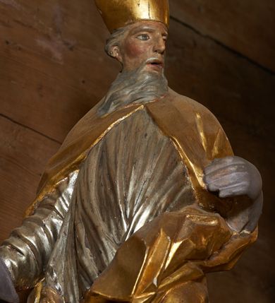 Zdjęcie nr 4: Rzeźba pełnoplastyczna, z tyłu drążona. Figura całopostaciowa, zwrócona en trois quarts w lewo, z głową skierowana w prawo, stojąca w kontrapoście i ekspresyjnym zwrocie ciała. Prawą ręką, wysuniętą w bok, podtrzymuje krzyż arcybiskupi, lewą ugiętą w łokciu trzyma połę kapy. Twarz szczupła, pociągła, o głęboko osadzonych oczach, dużym nosie i rozchylonych ustach, okolona długą, siwą brodą opadająca na pierś. Włosy krótkie, siwe, opadają na tył głowy. Święty ubrany w złoconą albę, srebrzoną komżę obficie drapowaną i skręconą wraz z postacią oraz ekspresyjnie rozwianą kapę, spiętą na piersi oraz zawiniętą na lewej nodze.