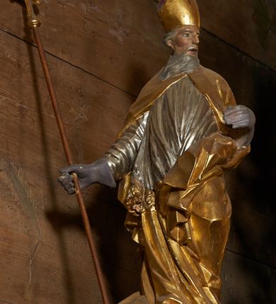 Zdjęcie nr 3: Rzeźba pełnoplastyczna, z tyłu drążona. Figura całopostaciowa, zwrócona en trois quarts w lewo, z głową skierowana w prawo, stojąca w kontrapoście i ekspresyjnym zwrocie ciała. Prawą ręką, wysuniętą w bok, podtrzymuje krzyż arcybiskupi, lewą ugiętą w łokciu trzyma połę kapy. Twarz szczupła, pociągła, o głęboko osadzonych oczach, dużym nosie i rozchylonych ustach, okolona długą, siwą brodą opadająca na pierś. Włosy krótkie, siwe, opadają na tył głowy. Święty ubrany w złoconą albę, srebrzoną komżę obficie drapowaną i skręconą wraz z postacią oraz ekspresyjnie rozwianą kapę, spiętą na piersi oraz zawiniętą na lewej nodze.