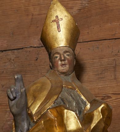 Zdjęcie nr 4: Rzeźba pełnoplastyczna, z tyłu drążona. Figura całopostaciowa, zwrócona en face do widza, stojąca w silnym kontrapoście, przechylona do tyłu. Prawą rękę wyciąga w geście błogosławieństwa, lewą odchyloną w bok, przytrzymuje pastorał. Twarz szczupła o wyraźnych rysach, głęboko osadzonych oczach, dużym nosie i niewielkich ustach. Na głowie infuła. Święty ubrany w złoconą albę, srebrzoną komżę, obficie drapowane, odpowiadające skrętowi sylwetki, oraz złoconą kapę spiętą na piersi, z ekspresyjnie rozwianym końcem przy prawym boku. Na dużych dłoniach rękawiczki. Przy prawej nodze świętego Piotrowin, ukazany w półpostaci, patrzący w górę, z rękami złożonymi w geście modlitwy.