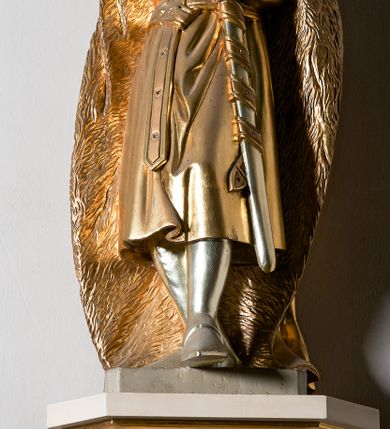 Zdjęcie nr 9: Pełnoplastyczna, drewniana figura św. Stefana, ustawiona na cokole na konsoli.  Święty został przedstawiony w pozycji stojącej, z lewą nogą wysuniętą nieco do przodu, ubrany w zapinany na guzki płaszcz i wysokie buty. Na to ma narzucony obfity płaszcz z futrzanym podbiciem spięty na prawym barku. Ma prosty nos i ciemne oczy. W prawej, uniesionej  ręce trzyma przed sobą krzyż, lewą opiera na rękojeści zatkniętego za pas miecza. Twarz pociągła, o wyrazistych rysach, okolona brodą. Spod zamkniętej korony spływają długie włosy opadające na oba ramiona i zwijające się w loki. Partie twarzy i włosów polichromowane naturalistycznie, szaty złocone.