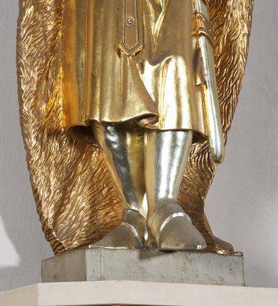 Zdjęcie nr 10: Pełnoplastyczna, drewniana figura św. Stefana, ustawiona na cokole na konsoli.  Święty został przedstawiony w pozycji stojącej, z lewą nogą wysuniętą nieco do przodu, ubrany w zapinany na guzki płaszcz i wysokie buty. Na to ma narzucony obfity płaszcz z futrzanym podbiciem spięty na prawym barku. Ma prosty nos i ciemne oczy. W prawej, uniesionej  ręce trzyma przed sobą krzyż, lewą opiera na rękojeści zatkniętego za pas miecza. Twarz pociągła, o wyrazistych rysach, okolona brodą. Spod zamkniętej korony spływają długie włosy opadające na oba ramiona i zwijające się w loki. Partie twarzy i włosów polichromowane naturalistycznie, szaty złocone.