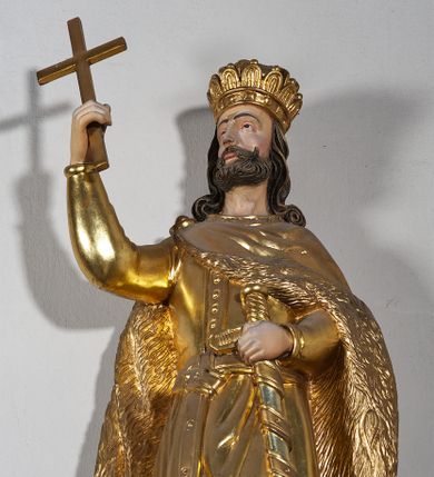 Zdjęcie nr 4: Pełnoplastyczna, drewniana figura św. Stefana, ustawiona na cokole na konsoli.  Święty został przedstawiony w pozycji stojącej, z lewą nogą wysuniętą nieco do przodu, ubrany w zapinany na guzki płaszcz i wysokie buty. Na to ma narzucony obfity płaszcz z futrzanym podbiciem spięty na prawym barku. Ma prosty nos i ciemne oczy. W prawej, uniesionej  ręce trzyma przed sobą krzyż, lewą opiera na rękojeści zatkniętego za pas miecza. Twarz pociągła, o wyrazistych rysach, okolona brodą. Spod zamkniętej korony spływają długie włosy opadające na oba ramiona i zwijające się w loki. Partie twarzy i włosów polichromowane naturalistycznie, szaty złocone.