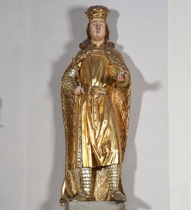 Zdjęcie nr 1: Pełnoplastyczna, drewniana figura św. Ludwika, ustawiona na konsoli. Święty został przedstawiony w pozycji stojącej, z lewą nogą wysuniętą nieco do przodu, ubrany w zbroję łuskową, na którą narzucono mu przewiązaną pasem tunikę i obfity płaszcz z futrzanym podbiciem spięty pod szyją. Prawą, ugiętą rękę opiera na biodrze, lewą wyciąga przed siebie. Twarz pociągła, okolona długimi włosami opadającymi na oba ramiona i zwijającymi się w loki. Ma niewielkie, pełne usta, prosty nos i ciemne oczy; na głowie korona zamknięta. Partie twarzy i włosów polichromowane naturalistycznie, szaty złocone. 