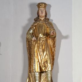 Zdjęcie nr 1: Pełnoplastyczna, drewniana figura św. Ludwika, ustawiona na konsoli. Święty został przedstawiony w pozycji stojącej, z lewą nogą wysuniętą nieco do przodu, ubrany w zbroję łuskową, na którą narzucono mu przewiązaną pasem tunikę i obfity płaszcz z futrzanym podbiciem spięty pod szyją. Prawą, ugiętą rękę opiera na biodrze, lewą wyciąga przed siebie. Twarz pociągła, okolona długimi włosami opadającymi na oba ramiona i zwijającymi się w loki. Ma niewielkie, pełne usta, prosty nos i ciemne oczy; na głowie korona zamknięta. Partie twarzy i włosów polichromowane naturalistycznie, szaty złocone. 