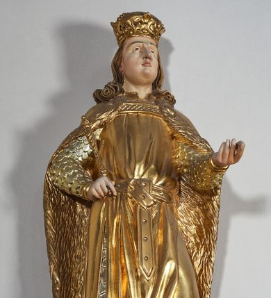Zdjęcie nr 3: Pełnoplastyczna, drewniana figura św. Ludwika, ustawiona na konsoli. Święty został przedstawiony w pozycji stojącej, z lewą nogą wysuniętą nieco do przodu, ubrany w zbroję łuskową, na którą narzucono mu przewiązaną pasem tunikę i obfity płaszcz z futrzanym podbiciem spięty pod szyją. Prawą, ugiętą rękę opiera na biodrze, lewą wyciąga przed siebie. Twarz pociągła, okolona długimi włosami opadającymi na oba ramiona i zwijającymi się w loki. Ma niewielkie, pełne usta, prosty nos i ciemne oczy; na głowie korona zamknięta. Partie twarzy i włosów polichromowane naturalistycznie, szaty złocone. 