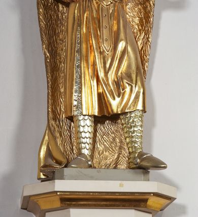 Zdjęcie nr 5: Pełnoplastyczna, drewniana figura św. Ludwika, ustawiona na konsoli. Święty został przedstawiony w pozycji stojącej, z lewą nogą wysuniętą nieco do przodu, ubrany w zbroję łuskową, na którą narzucono mu przewiązaną pasem tunikę i obfity płaszcz z futrzanym podbiciem spięty pod szyją. Prawą, ugiętą rękę opiera na biodrze, lewą wyciąga przed siebie. Twarz pociągła, okolona długimi włosami opadającymi na oba ramiona i zwijającymi się w loki. Ma niewielkie, pełne usta, prosty nos i ciemne oczy; na głowie korona zamknięta. Partie twarzy i włosów polichromowane naturalistycznie, szaty złocone. 