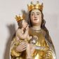 Zdjęcie nr 1: Rzeźba pełna, na cokole, przedstawiająca Matkę Boską z Dzieciątkiem. Maria przytrzymuje Jezusa prawą ręką, lewą opuszcza przed sobą, patrzy na wprost. Ma podłużną, pełną twarz z małymi, ciemnymi oczami, prostym nosem i szerokimi ustami. Jest ubrana z złotą suknię ze srebrnym paskiem, która drobnymi fałdami łamie się na wysokości stóp i złoty płaszcz ze srebrnym podbiciem, który wywija się na krawędziach.  Dzieciątko siedzi, patrzy na Matkę, prawą ręką błogosławi, w lewej trzyma jabłko królewskie, jest owinięte w pasie złotą szarfą. Obie postacie mają na głowach złote, otwarte korony. Polichromia w partiach ciała naturalistyczna. 