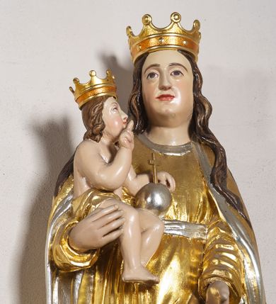 Zdjęcie nr 1: Rzeźba pełna, na cokole, przedstawiająca Matkę Boską z Dzieciątkiem. Maria przytrzymuje Jezusa prawą ręką, lewą opuszcza przed sobą, patrzy na wprost. Ma podłużną, pełną twarz z małymi, ciemnymi oczami, prostym nosem i szerokimi ustami. Jest ubrana z złotą suknię ze srebrnym paskiem, która drobnymi fałdami łamie się na wysokości stóp i złoty płaszcz ze srebrnym podbiciem, który wywija się na krawędziach.  Dzieciątko siedzi, patrzy na Matkę, prawą ręką błogosławi, w lewej trzyma jabłko królewskie, jest owinięte w pasie złotą szarfą. Obie postacie mają na głowach złote, otwarte korony. Polichromia w partiach ciała naturalistyczna. 