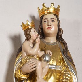 Zdjęcie nr 1: Rzeźba pełna, na cokole, przedstawiająca Matkę Boską z Dzieciątkiem. Maria przytrzymuje Jezusa prawą ręką, lewą opuszcza przed sobą, patrzy na wprost. Ma podłużną, pełną twarz z małymi, ciemnymi oczami, prostym nosem i szerokimi ustami. Jest ubrana z złotą suknię ze srebrnym paskiem, która drobnymi fałdami łamie się na wysokości stóp i złoty płaszcz ze srebrnym podbiciem, który wywija się na krawędziach.  Dzieciątko siedzi, patrzy na Matkę, prawą ręką błogosławi, w lewej trzyma jabłko królewskie, jest owinięte w pasie złotą szarfą. Obie postacie mają na głowach złote, otwarte korony. Polichromia w partiach ciała naturalistyczna. 