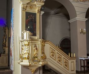 Zdjęcie nr 1: Ambona przyścienna, wisząca, dostępna schodami z podestem. Ich balustrada jest pełna dekorowana płycinami wypełnionymi plakietami z ornamentacją roślinną. Kosz na profilowanym cokole z półwałkiem, na planie prostokąta o wklęsło-wypukłych ściankach wydzielonych spływami z wolutami, dekorowanymi kampanulami i liśćmi akantu. Na wklęsłych ściankach płyciny w kształcie stojącego prostokąta, wypełnione płaskorzeźbionymi, całopostaciowymi przedstawieniami św. Łukasza z lewej i św. Jana Ewangelisty z prawej strony, pod ich stopami kartusze ujęte dekoracją rocaille’ową.  Parapet w postaci profilowanego gzymsu wyłamanego nad spływami. Spód kosza w kształcie wklęsło-wypukłego, odwróconego stożka zakończonego szyszką. Zaplecek w formie wydłużonego prostokąta ujętego kanelowanymi pilastrami. W polu obraz w kształcie stojącego prostokąta z wizerunkiem Chrystusa Dobrego Pasterza. Pilastry podtrzymują profilowane belkowanie wyłamane na ich osiach, na których znajdują się fragmenty przyczółka skierowane na zewnątrz. Między nimi, na ścianie rozbudowane przedstawienie gołębicy Ducha Świętego na tle glorii promienistej  i obłoków.  Struktura w odcieniu kremowym, dekoracja i profile złocone i srebrzone. 