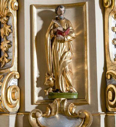 Zdjęcie nr 8: Ambona przyścienna, wisząca, dostępna schodami z podestem. Ich balustrada jest pełna dekorowana płycinami wypełnionymi plakietami z ornamentacją roślinną. Kosz na profilowanym cokole z półwałkiem, na planie prostokąta o wklęsło-wypukłych ściankach wydzielonych spływami z wolutami, dekorowanymi kampanulami i liśćmi akantu. Na wklęsłych ściankach płyciny w kształcie stojącego prostokąta, wypełnione płaskorzeźbionymi, całopostaciowymi przedstawieniami św. Łukasza z lewej i św. Jana Ewangelisty z prawej strony, pod ich stopami kartusze ujęte dekoracją rocaille’ową.  Parapet w postaci profilowanego gzymsu wyłamanego nad spływami. Spód kosza w kształcie wklęsło-wypukłego, odwróconego stożka zakończonego szyszką. Zaplecek w formie wydłużonego prostokąta ujętego kanelowanymi pilastrami. W polu obraz w kształcie stojącego prostokąta z wizerunkiem Chrystusa Dobrego Pasterza. Pilastry podtrzymują profilowane belkowanie wyłamane na ich osiach, na których znajdują się fragmenty przyczółka skierowane na zewnątrz. Między nimi, na ścianie rozbudowane przedstawienie gołębicy Ducha Świętego na tle glorii promienistej  i obłoków.  Struktura w odcieniu kremowym, dekoracja i profile złocone i srebrzone. 