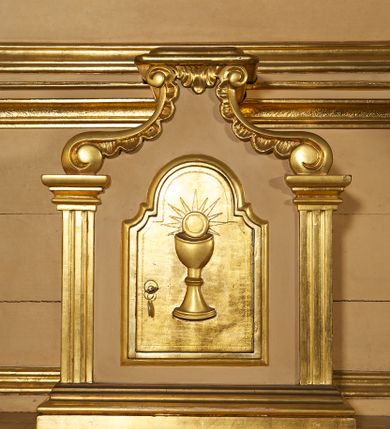 Zdjęcie nr 23: Ołtarz przyścienny, architektoniczny, jednoosiowy, jednokondygnacyjny ze zwieńczeniem. Mensa prostopadłościenna na profilowanym cokole, antepedium dekorowane trzema płycinami z plakietami z ornamentu roślinnego. Tabernakulum architektoniczne, w formie prostopadłościanu na profilowanym cokole, o ujętym wolutami wklęsło-wypukłym zwieńczeniu. Na ścianie frontowej drzwiczki w kształcie stojącego prostokąta zamkniętego łukiem nadwieszonym z uskokiem. Nastawa ołtarzowa ujęta  pilastrami z płycinami ustawionymi na wysokich cokołach, na których wspierają się konsole podtrzymujące rzeźby aniołów. Podpory dźwigają pełne, wyłamane na ich osiach belkowanie, na którym posadowiono figury aniołków. W centrum kondygnacji prostokątna nisza mieszcząca obraz „Męczeństwo św. Bartłomieja”, ujęta prostokątną ramą dekorowaną w czterech miejscach kwitnącymi różami z liśćmi. Między polem obrazowym a belkowaniem kondygnacji unoszony przez dwa anioły kartusz z inskrypcją „ŚWIĘTY / BARTŁOMIEJU / MÓDL SIĘ / ZA NAMI”. Zwieńczenie o kształcie wklęsło-wypukłym, ujęte ulistnionymi wolutami, wypełnione obrazem powtarzającym jego kształt, przedstawiającym Jezusa Chrystusa. Na szczycie krzyż równoramienny o ramionach zakończonych trójlistnie, na tle glorii.  Struktura ołtarza w kolorze kremowym; profile, detale i ornamenty złocone i srebrzone.