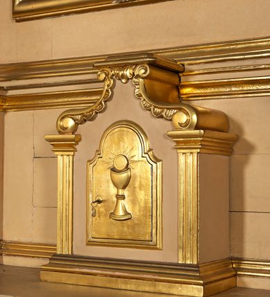 Zdjęcie nr 24: Ołtarz przyścienny, architektoniczny, jednoosiowy, jednokondygnacyjny ze zwieńczeniem. Mensa prostopadłościenna na profilowanym cokole, antepedium dekorowane trzema płycinami z plakietami z ornamentu roślinnego. Tabernakulum architektoniczne, w formie prostopadłościanu na profilowanym cokole, o ujętym wolutami wklęsło-wypukłym zwieńczeniu. Na ścianie frontowej drzwiczki w kształcie stojącego prostokąta zamkniętego łukiem nadwieszonym z uskokiem. Nastawa ołtarzowa ujęta  pilastrami z płycinami ustawionymi na wysokich cokołach, na których wspierają się konsole podtrzymujące rzeźby aniołów. Podpory dźwigają pełne, wyłamane na ich osiach belkowanie, na którym posadowiono figury aniołków. W centrum kondygnacji prostokątna nisza mieszcząca obraz „Męczeństwo św. Bartłomieja”, ujęta prostokątną ramą dekorowaną w czterech miejscach kwitnącymi różami z liśćmi. Między polem obrazowym a belkowaniem kondygnacji unoszony przez dwa anioły kartusz z inskrypcją „ŚWIĘTY / BARTŁOMIEJU / MÓDL SIĘ / ZA NAMI”. Zwieńczenie o kształcie wklęsło-wypukłym, ujęte ulistnionymi wolutami, wypełnione obrazem powtarzającym jego kształt, przedstawiającym Jezusa Chrystusa. Na szczycie krzyż równoramienny o ramionach zakończonych trójlistnie, na tle glorii.  Struktura ołtarza w kolorze kremowym; profile, detale i ornamenty złocone i srebrzone.