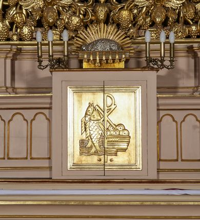 Zdjęcie nr 31: Ołtarz w formie rzeźbionej, ażurowej ramy na trójstopniowym cokole, z prostopadłościenną mensą z antepedium dekorowanym kwadratowymi płycinami z motywem czworoliścia. Na nim prostopadłościenne tabernakulum z drzwiami w kształcie stojącego prostokąta dekorowanymi koszem z chlebem, rybami i chrystogramem. Środkowa część podstawy wypełniona płycinami w kształcie leżących prostokątów z plakietami roślinnymi. Na jej zewnętrznych częściach posadowiono figury klęczących aniołów. Najwyższy stopień węższy, trójosiowy, o osiach zewnętrznych wysuniętych, flankowany konsolami z rzeźbami Matki Boskiej po lewej stronie i św. Jana Ewangelisty po prawej. Centralnie umieszczona rama ujmuje pole w kształcie serca, na tle którego jest eksponowany krucyfiks. Ażur tworzy wić winnej latorośli z kiśćmi winogron, a w nią wkomponowane jest siedem postaci aniołów trzymających banderole z ostatnimi słowami wypowiedzianymi przez Chrystusa wiszącego na krzyżu. Od góry: „Pragnę”, „Niewiasto! Oto syn Twój”, „Oto matka twoja”, „Ojcze odpuść im, / bo nie wiedzą co czynią”, „Zaprawdę powiadam tobie / dziś jeszcze będziesz ze Mną w raju”, „Spełniło się! / Ojcze w ręce Twoje oddaję ducha mojego”, „Boże mój Boże mój / czemużeś mnie opuścił”. Struktura w kolorze kremowym, profile, detale i ornamenty złocone; banderole srebrzone. 