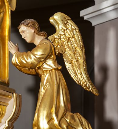 Zdjęcie nr 14: Ołtarz w formie rzeźbionej, ażurowej ramy na trójstopniowym cokole, z prostopadłościenną mensą z antepedium dekorowanym kwadratowymi płycinami z motywem czworoliścia. Na nim prostopadłościenne tabernakulum z drzwiami w kształcie stojącego prostokąta dekorowanymi koszem z chlebem, rybami i chrystogramem. Środkowa część podstawy wypełniona płycinami w kształcie leżących prostokątów z plakietami roślinnymi. Na jej zewnętrznych częściach posadowiono figury klęczących aniołów. Najwyższy stopień węższy, trójosiowy, o osiach zewnętrznych wysuniętych, flankowany konsolami z rzeźbami Matki Boskiej po lewej stronie i św. Jana Ewangelisty po prawej. Centralnie umieszczona rama ujmuje pole w kształcie serca, na tle którego jest eksponowany krucyfiks. Ażur tworzy wić winnej latorośli z kiśćmi winogron, a w nią wkomponowane jest siedem postaci aniołów trzymających banderole z ostatnimi słowami wypowiedzianymi przez Chrystusa wiszącego na krzyżu. Od góry: „Pragnę”, „Niewiasto! Oto syn Twój”, „Oto matka twoja”, „Ojcze odpuść im, / bo nie wiedzą co czynią”, „Zaprawdę powiadam tobie / dziś jeszcze będziesz ze Mną w raju”, „Spełniło się! / Ojcze w ręce Twoje oddaję ducha mojego”, „Boże mój Boże mój / czemużeś mnie opuścił”. Struktura w kolorze kremowym, profile, detale i ornamenty złocone; banderole srebrzone. 