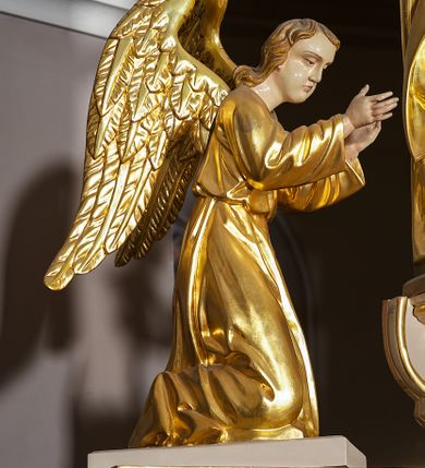 Zdjęcie nr 18: Ołtarz w formie rzeźbionej, ażurowej ramy na trójstopniowym cokole, z prostopadłościenną mensą z antepedium dekorowanym kwadratowymi płycinami z motywem czworoliścia. Na nim prostopadłościenne tabernakulum z drzwiami w kształcie stojącego prostokąta dekorowanymi koszem z chlebem, rybami i chrystogramem. Środkowa część podstawy wypełniona płycinami w kształcie leżących prostokątów z plakietami roślinnymi. Na jej zewnętrznych częściach posadowiono figury klęczących aniołów. Najwyższy stopień węższy, trójosiowy, o osiach zewnętrznych wysuniętych, flankowany konsolami z rzeźbami Matki Boskiej po lewej stronie i św. Jana Ewangelisty po prawej. Centralnie umieszczona rama ujmuje pole w kształcie serca, na tle którego jest eksponowany krucyfiks. Ażur tworzy wić winnej latorośli z kiśćmi winogron, a w nią wkomponowane jest siedem postaci aniołów trzymających banderole z ostatnimi słowami wypowiedzianymi przez Chrystusa wiszącego na krzyżu. Od góry: „Pragnę”, „Niewiasto! Oto syn Twój”, „Oto matka twoja”, „Ojcze odpuść im, / bo nie wiedzą co czynią”, „Zaprawdę powiadam tobie / dziś jeszcze będziesz ze Mną w raju”, „Spełniło się! / Ojcze w ręce Twoje oddaję ducha mojego”, „Boże mój Boże mój / czemużeś mnie opuścił”. Struktura w kolorze kremowym, profile, detale i ornamenty złocone; banderole srebrzone. 