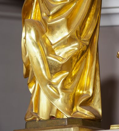 Zdjęcie nr 28: Ołtarz w formie rzeźbionej, ażurowej ramy na trójstopniowym cokole, z prostopadłościenną mensą z antepedium dekorowanym kwadratowymi płycinami z motywem czworoliścia. Na nim prostopadłościenne tabernakulum z drzwiami w kształcie stojącego prostokąta dekorowanymi koszem z chlebem, rybami i chrystogramem. Środkowa część podstawy wypełniona płycinami w kształcie leżących prostokątów z plakietami roślinnymi. Na jej zewnętrznych częściach posadowiono figury klęczących aniołów. Najwyższy stopień węższy, trójosiowy, o osiach zewnętrznych wysuniętych, flankowany konsolami z rzeźbami Matki Boskiej po lewej stronie i św. Jana Ewangelisty po prawej. Centralnie umieszczona rama ujmuje pole w kształcie serca, na tle którego jest eksponowany krucyfiks. Ażur tworzy wić winnej latorośli z kiśćmi winogron, a w nią wkomponowane jest siedem postaci aniołów trzymających banderole z ostatnimi słowami wypowiedzianymi przez Chrystusa wiszącego na krzyżu. Od góry: „Pragnę”, „Niewiasto! Oto syn Twój”, „Oto matka twoja”, „Ojcze odpuść im, / bo nie wiedzą co czynią”, „Zaprawdę powiadam tobie / dziś jeszcze będziesz ze Mną w raju”, „Spełniło się! / Ojcze w ręce Twoje oddaję ducha mojego”, „Boże mój Boże mój / czemużeś mnie opuścił”. Struktura w kolorze kremowym, profile, detale i ornamenty złocone; banderole srebrzone. 