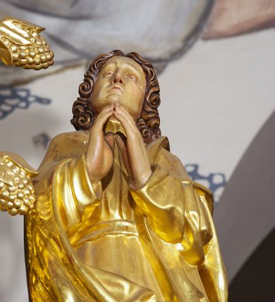 Zdjęcie nr 22: Ołtarz w formie rzeźbionej, ażurowej ramy na trójstopniowym cokole, z prostopadłościenną mensą z antepedium dekorowanym kwadratowymi płycinami z motywem czworoliścia. Na nim prostopadłościenne tabernakulum z drzwiami w kształcie stojącego prostokąta dekorowanymi koszem z chlebem, rybami i chrystogramem. Środkowa część podstawy wypełniona płycinami w kształcie leżących prostokątów z plakietami roślinnymi. Na jej zewnętrznych częściach posadowiono figury klęczących aniołów. Najwyższy stopień węższy, trójosiowy, o osiach zewnętrznych wysuniętych, flankowany konsolami z rzeźbami Matki Boskiej po lewej stronie i św. Jana Ewangelisty po prawej. Centralnie umieszczona rama ujmuje pole w kształcie serca, na tle którego jest eksponowany krucyfiks. Ażur tworzy wić winnej latorośli z kiśćmi winogron, a w nią wkomponowane jest siedem postaci aniołów trzymających banderole z ostatnimi słowami wypowiedzianymi przez Chrystusa wiszącego na krzyżu. Od góry: „Pragnę”, „Niewiasto! Oto syn Twój”, „Oto matka twoja”, „Ojcze odpuść im, / bo nie wiedzą co czynią”, „Zaprawdę powiadam tobie / dziś jeszcze będziesz ze Mną w raju”, „Spełniło się! / Ojcze w ręce Twoje oddaję ducha mojego”, „Boże mój Boże mój / czemużeś mnie opuścił”. Struktura w kolorze kremowym, profile, detale i ornamenty złocone; banderole srebrzone. 