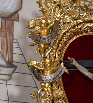 Zdjęcie nr 9: Ołtarz w formie rzeźbionej, ażurowej ramy na trójstopniowym cokole, z prostopadłościenną mensą z antepedium dekorowanym kwadratowymi płycinami z motywem czworoliścia. Na nim prostopadłościenne tabernakulum z drzwiami w kształcie stojącego prostokąta dekorowanymi koszem z chlebem, rybami i chrystogramem. Środkowa część podstawy wypełniona płycinami w kształcie leżących prostokątów z plakietami roślinnymi. Na jej zewnętrznych częściach posadowiono figury klęczących aniołów. Najwyższy stopień węższy, trójosiowy, o osiach zewnętrznych wysuniętych, flankowany konsolami z rzeźbami Matki Boskiej po lewej stronie i św. Jana Ewangelisty po prawej. Centralnie umieszczona rama ujmuje pole w kształcie serca, na tle którego jest eksponowany krucyfiks. Ażur tworzy wić winnej latorośli z kiśćmi winogron, a w nią wkomponowane jest siedem postaci aniołów trzymających banderole z ostatnimi słowami wypowiedzianymi przez Chrystusa wiszącego na krzyżu. Od góry: „Pragnę”, „Niewiasto! Oto syn Twój”, „Oto matka twoja”, „Ojcze odpuść im, / bo nie wiedzą co czynią”, „Zaprawdę powiadam tobie / dziś jeszcze będziesz ze Mną w raju”, „Spełniło się! / Ojcze w ręce Twoje oddaję ducha mojego”, „Boże mój Boże mój / czemużeś mnie opuścił”. Struktura w kolorze kremowym, profile, detale i ornamenty złocone; banderole srebrzone. 