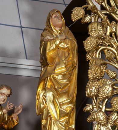 Zdjęcie nr 25: Ołtarz w formie rzeźbionej, ażurowej ramy na trójstopniowym cokole, z prostopadłościenną mensą z antepedium dekorowanym kwadratowymi płycinami z motywem czworoliścia. Na nim prostopadłościenne tabernakulum z drzwiami w kształcie stojącego prostokąta dekorowanymi koszem z chlebem, rybami i chrystogramem. Środkowa część podstawy wypełniona płycinami w kształcie leżących prostokątów z plakietami roślinnymi. Na jej zewnętrznych częściach posadowiono figury klęczących aniołów. Najwyższy stopień węższy, trójosiowy, o osiach zewnętrznych wysuniętych, flankowany konsolami z rzeźbami Matki Boskiej po lewej stronie i św. Jana Ewangelisty po prawej. Centralnie umieszczona rama ujmuje pole w kształcie serca, na tle którego jest eksponowany krucyfiks. Ażur tworzy wić winnej latorośli z kiśćmi winogron, a w nią wkomponowane jest siedem postaci aniołów trzymających banderole z ostatnimi słowami wypowiedzianymi przez Chrystusa wiszącego na krzyżu. Od góry: „Pragnę”, „Niewiasto! Oto syn Twój”, „Oto matka twoja”, „Ojcze odpuść im, / bo nie wiedzą co czynią”, „Zaprawdę powiadam tobie / dziś jeszcze będziesz ze Mną w raju”, „Spełniło się! / Ojcze w ręce Twoje oddaję ducha mojego”, „Boże mój Boże mój / czemużeś mnie opuścił”. Struktura w kolorze kremowym, profile, detale i ornamenty złocone; banderole srebrzone. 