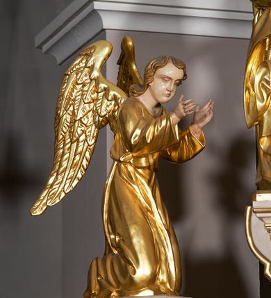 Zdjęcie nr 19: Ołtarz w formie rzeźbionej, ażurowej ramy na trójstopniowym cokole, z prostopadłościenną mensą z antepedium dekorowanym kwadratowymi płycinami z motywem czworoliścia. Na nim prostopadłościenne tabernakulum z drzwiami w kształcie stojącego prostokąta dekorowanymi koszem z chlebem, rybami i chrystogramem. Środkowa część podstawy wypełniona płycinami w kształcie leżących prostokątów z plakietami roślinnymi. Na jej zewnętrznych częściach posadowiono figury klęczących aniołów. Najwyższy stopień węższy, trójosiowy, o osiach zewnętrznych wysuniętych, flankowany konsolami z rzeźbami Matki Boskiej po lewej stronie i św. Jana Ewangelisty po prawej. Centralnie umieszczona rama ujmuje pole w kształcie serca, na tle którego jest eksponowany krucyfiks. Ażur tworzy wić winnej latorośli z kiśćmi winogron, a w nią wkomponowane jest siedem postaci aniołów trzymających banderole z ostatnimi słowami wypowiedzianymi przez Chrystusa wiszącego na krzyżu. Od góry: „Pragnę”, „Niewiasto! Oto syn Twój”, „Oto matka twoja”, „Ojcze odpuść im, / bo nie wiedzą co czynią”, „Zaprawdę powiadam tobie / dziś jeszcze będziesz ze Mną w raju”, „Spełniło się! / Ojcze w ręce Twoje oddaję ducha mojego”, „Boże mój Boże mój / czemużeś mnie opuścił”. Struktura w kolorze kremowym, profile, detale i ornamenty złocone; banderole srebrzone. 