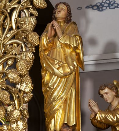 Zdjęcie nr 21: Ołtarz w formie rzeźbionej, ażurowej ramy na trójstopniowym cokole, z prostopadłościenną mensą z antepedium dekorowanym kwadratowymi płycinami z motywem czworoliścia. Na nim prostopadłościenne tabernakulum z drzwiami w kształcie stojącego prostokąta dekorowanymi koszem z chlebem, rybami i chrystogramem. Środkowa część podstawy wypełniona płycinami w kształcie leżących prostokątów z plakietami roślinnymi. Na jej zewnętrznych częściach posadowiono figury klęczących aniołów. Najwyższy stopień węższy, trójosiowy, o osiach zewnętrznych wysuniętych, flankowany konsolami z rzeźbami Matki Boskiej po lewej stronie i św. Jana Ewangelisty po prawej. Centralnie umieszczona rama ujmuje pole w kształcie serca, na tle którego jest eksponowany krucyfiks. Ażur tworzy wić winnej latorośli z kiśćmi winogron, a w nią wkomponowane jest siedem postaci aniołów trzymających banderole z ostatnimi słowami wypowiedzianymi przez Chrystusa wiszącego na krzyżu. Od góry: „Pragnę”, „Niewiasto! Oto syn Twój”, „Oto matka twoja”, „Ojcze odpuść im, / bo nie wiedzą co czynią”, „Zaprawdę powiadam tobie / dziś jeszcze będziesz ze Mną w raju”, „Spełniło się! / Ojcze w ręce Twoje oddaję ducha mojego”, „Boże mój Boże mój / czemużeś mnie opuścił”. Struktura w kolorze kremowym, profile, detale i ornamenty złocone; banderole srebrzone. 