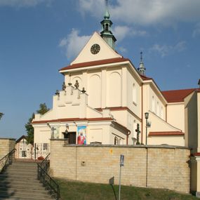 Zdjęcie nr 1: Kościół murowany, orientowany, jednonawowy, z transeptem, prezbiterium z obejściem i przybudówkami. Od zachodu kruchta, od północy kwadratowa kaplica, od południa kolejna przybudówka. 
Prezbiterium zamknięte półokrągło, z obejściem przeprutym do niego arkadami wspartymi na filarach. Ściany nawy i prezbiterium gładkie, przekryte sklepieniem kolebkowym z lunetami, w których mieszczą się okna. Transept i przecięcie naw sklepione krzyżowo. Na ścianach polichromia figuralna ze scenami z Nowego Testamentu, w partii sklepienia drobne, złote gwiazdki. Od zachodu chór zatopiony w występującym asymetrycznie murze, z tralkową balustradą. W prezbiterium siedem okien w kształcie stojącego prostokąta zamkniętego łukiem pełnym wypełnionych witrażami, w nawie sześć okien, w ramionach transeptu po jednym, czterodzielnym, wypełnionym witrażem, na wysokości chóru po dwa z każdej strony. Główne wejście od zachodu przez kruchtę. Fasada poprzedzona przedsionkiem o podziałach ramowych, z prostokątnym wejściem na osi, flankowanym parą pilastrów i prostokątnymi płycinami. Kondygnację wieńczy pełne belkowanie z wysuniętym gzymsem podtrzymującym daszek i trójkątny, schodkowy szczyt zakończony postumentami. Na centralnym krzyż, na sąsiadujących figury dzieci z rogami obfitości, a na zewnętrznych wazony płomieniste; szczyt ujmują postumenty z kulami. Fasada dwukondygnacyjna ze szczytem. Kondygnacja trójosiowa, rozdzielona pilastrami, o polach wypełnionych blendami w kształcie stojących prostokątów zamkniętych łukiem pełnym; szczyt trójkątny, z tarczą zegarową pośrodku. Budynek kościoła o wyraźnych podziałach na bryły składowe, ściany gładkie, przeprute oknami, z gzymsami pod krawędziami dachu. 
Nad nawą główną, na kalenicy, wieżyczka na sygnaturkę z latarnią i baniastym hełmem, druga na skrzyżowaniu naw, z latarnią i  hełmem zakończonym krzyżem. Dach nad nawą główną i przedsionkiem dwuspadowy, nad ramionami transeptu trójspadowym,nad prezbiterium zakończony wielobocznie, na przybudówkach dachy pulpitowe, dwuspadowe i wielospadowe. Dachy kryte dachówką ceramiczną, wieżyczki blachą. 
Najciekawszymi zabytkami kościoła są ołtarz główny z około 1700 roku z nastawą utworzoną z wici winnej latorośli, manierystyczny ołtarz boczny oraz siedemnastowieczna chrzcielnica z warsztatu Santi Gucciego. 
