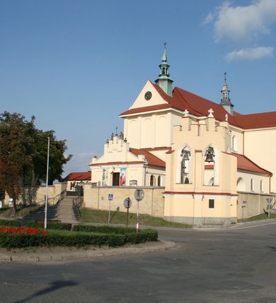 Zdjęcie nr 112: Kościół murowany, orientowany, jednonawowy, z transeptem, prezbiterium z obejściem i przybudówkami. Od zachodu kruchta, od północy kwadratowa kaplica, od południa kolejna przybudówka. 
Prezbiterium zamknięte półokrągło, z obejściem przeprutym do niego arkadami wspartymi na filarach. Ściany nawy i prezbiterium gładkie, przekryte sklepieniem kolebkowym z lunetami, w których mieszczą się okna. Transept i przecięcie naw sklepione krzyżowo. Na ścianach polichromia figuralna ze scenami z Nowego Testamentu, w partii sklepienia drobne, złote gwiazdki. Od zachodu chór zatopiony w występującym asymetrycznie murze, z tralkową balustradą. W prezbiterium siedem okien w kształcie stojącego prostokąta zamkniętego łukiem pełnym wypełnionych witrażami, w nawie sześć okien, w ramionach transeptu po jednym, czterodzielnym, wypełnionym witrażem, na wysokości chóru po dwa z każdej strony. Główne wejście od zachodu przez kruchtę. Fasada poprzedzona przedsionkiem o podziałach ramowych, z prostokątnym wejściem na osi, flankowanym parą pilastrów i prostokątnymi płycinami. Kondygnację wieńczy pełne belkowanie z wysuniętym gzymsem podtrzymującym daszek i trójkątny, schodkowy szczyt zakończony postumentami. Na centralnym krzyż, na sąsiadujących figury dzieci z rogami obfitości, a na zewnętrznych wazony płomieniste; szczyt ujmują postumenty z kulami. Fasada dwukondygnacyjna ze szczytem. Kondygnacja trójosiowa, rozdzielona pilastrami, o polach wypełnionych blendami w kształcie stojących prostokątów zamkniętych łukiem pełnym; szczyt trójkątny, z tarczą zegarową pośrodku. Budynek kościoła o wyraźnych podziałach na bryły składowe, ściany gładkie, przeprute oknami, z gzymsami pod krawędziami dachu. 
Nad nawą główną, na kalenicy, wieżyczka na sygnaturkę z latarnią i baniastym hełmem, druga na skrzyżowaniu naw, z latarnią i  hełmem zakończonym krzyżem. Dach nad nawą główną i przedsionkiem dwuspadowy, nad ramionami transeptu trójspadowym,nad prezbiterium zakończony wielobocznie, na przybudówkach dachy pulpitowe, dwuspadowe i wielospadowe. Dachy kryte dachówką ceramiczną, wieżyczki blachą. 
Najciekawszymi zabytkami kościoła są ołtarz główny z około 1700 roku z nastawą utworzoną z wici winnej latorośli, manierystyczny ołtarz boczny oraz siedemnastowieczna chrzcielnica z warsztatu Santi Gucciego. 
