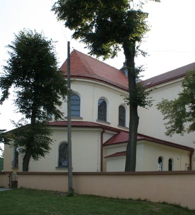 Zdjęcie nr 154: Kościół murowany, orientowany, jednonawowy, z transeptem, prezbiterium z obejściem i przybudówkami. Od zachodu kruchta, od północy kwadratowa kaplica, od południa kolejna przybudówka. 
Prezbiterium zamknięte półokrągło, z obejściem przeprutym do niego arkadami wspartymi na filarach. Ściany nawy i prezbiterium gładkie, przekryte sklepieniem kolebkowym z lunetami, w których mieszczą się okna. Transept i przecięcie naw sklepione krzyżowo. Na ścianach polichromia figuralna ze scenami z Nowego Testamentu, w partii sklepienia drobne, złote gwiazdki. Od zachodu chór zatopiony w występującym asymetrycznie murze, z tralkową balustradą. W prezbiterium siedem okien w kształcie stojącego prostokąta zamkniętego łukiem pełnym wypełnionych witrażami, w nawie sześć okien, w ramionach transeptu po jednym, czterodzielnym, wypełnionym witrażem, na wysokości chóru po dwa z każdej strony. Główne wejście od zachodu przez kruchtę. Fasada poprzedzona przedsionkiem o podziałach ramowych, z prostokątnym wejściem na osi, flankowanym parą pilastrów i prostokątnymi płycinami. Kondygnację wieńczy pełne belkowanie z wysuniętym gzymsem podtrzymującym daszek i trójkątny, schodkowy szczyt zakończony postumentami. Na centralnym krzyż, na sąsiadujących figury dzieci z rogami obfitości, a na zewnętrznych wazony płomieniste; szczyt ujmują postumenty z kulami. Fasada dwukondygnacyjna ze szczytem. Kondygnacja trójosiowa, rozdzielona pilastrami, o polach wypełnionych blendami w kształcie stojących prostokątów zamkniętych łukiem pełnym; szczyt trójkątny, z tarczą zegarową pośrodku. Budynek kościoła o wyraźnych podziałach na bryły składowe, ściany gładkie, przeprute oknami, z gzymsami pod krawędziami dachu. 
Nad nawą główną, na kalenicy, wieżyczka na sygnaturkę z latarnią i baniastym hełmem, druga na skrzyżowaniu naw, z latarnią i  hełmem zakończonym krzyżem. Dach nad nawą główną i przedsionkiem dwuspadowy, nad ramionami transeptu trójspadowym,nad prezbiterium zakończony wielobocznie, na przybudówkach dachy pulpitowe, dwuspadowe i wielospadowe. Dachy kryte dachówką ceramiczną, wieżyczki blachą. 
Najciekawszymi zabytkami kościoła są ołtarz główny z około 1700 roku z nastawą utworzoną z wici winnej latorośli, manierystyczny ołtarz boczny oraz siedemnastowieczna chrzcielnica z warsztatu Santi Gucciego. 
