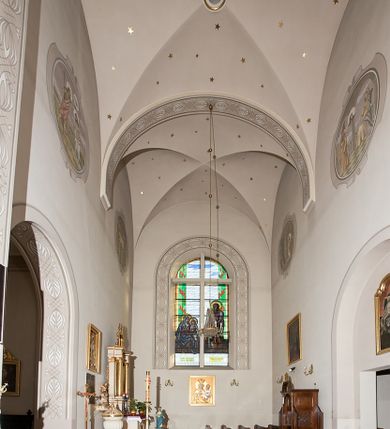 Zdjęcie nr 152: Kościół murowany, orientowany, jednonawowy, z transeptem, prezbiterium z obejściem i przybudówkami. Od zachodu kruchta, od północy kwadratowa kaplica, od południa kolejna przybudówka. 
Prezbiterium zamknięte półokrągło, z obejściem przeprutym do niego arkadami wspartymi na filarach. Ściany nawy i prezbiterium gładkie, przekryte sklepieniem kolebkowym z lunetami, w których mieszczą się okna. Transept i przecięcie naw sklepione krzyżowo. Na ścianach polichromia figuralna ze scenami z Nowego Testamentu, w partii sklepienia drobne, złote gwiazdki. Od zachodu chór zatopiony w występującym asymetrycznie murze, z tralkową balustradą. W prezbiterium siedem okien w kształcie stojącego prostokąta zamkniętego łukiem pełnym wypełnionych witrażami, w nawie sześć okien, w ramionach transeptu po jednym, czterodzielnym, wypełnionym witrażem, na wysokości chóru po dwa z każdej strony. Główne wejście od zachodu przez kruchtę. Fasada poprzedzona przedsionkiem o podziałach ramowych, z prostokątnym wejściem na osi, flankowanym parą pilastrów i prostokątnymi płycinami. Kondygnację wieńczy pełne belkowanie z wysuniętym gzymsem podtrzymującym daszek i trójkątny, schodkowy szczyt zakończony postumentami. Na centralnym krzyż, na sąsiadujących figury dzieci z rogami obfitości, a na zewnętrznych wazony płomieniste; szczyt ujmują postumenty z kulami. Fasada dwukondygnacyjna ze szczytem. Kondygnacja trójosiowa, rozdzielona pilastrami, o polach wypełnionych blendami w kształcie stojących prostokątów zamkniętych łukiem pełnym; szczyt trójkątny, z tarczą zegarową pośrodku. Budynek kościoła o wyraźnych podziałach na bryły składowe, ściany gładkie, przeprute oknami, z gzymsami pod krawędziami dachu. 
Nad nawą główną, na kalenicy, wieżyczka na sygnaturkę z latarnią i baniastym hełmem, druga na skrzyżowaniu naw, z latarnią i  hełmem zakończonym krzyżem. Dach nad nawą główną i przedsionkiem dwuspadowy, nad ramionami transeptu trójspadowym,nad prezbiterium zakończony wielobocznie, na przybudówkach dachy pulpitowe, dwuspadowe i wielospadowe. Dachy kryte dachówką ceramiczną, wieżyczki blachą. 
Najciekawszymi zabytkami kościoła są ołtarz główny z około 1700 roku z nastawą utworzoną z wici winnej latorośli, manierystyczny ołtarz boczny oraz siedemnastowieczna chrzcielnica z warsztatu Santi Gucciego. 
