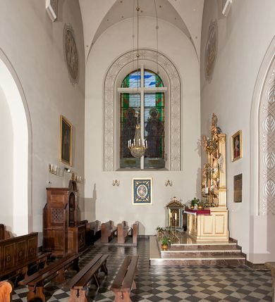 Zdjęcie nr 153: Kościół murowany, orientowany, jednonawowy, z transeptem, prezbiterium z obejściem i przybudówkami. Od zachodu kruchta, od północy kwadratowa kaplica, od południa kolejna przybudówka. 
Prezbiterium zamknięte półokrągło, z obejściem przeprutym do niego arkadami wspartymi na filarach. Ściany nawy i prezbiterium gładkie, przekryte sklepieniem kolebkowym z lunetami, w których mieszczą się okna. Transept i przecięcie naw sklepione krzyżowo. Na ścianach polichromia figuralna ze scenami z Nowego Testamentu, w partii sklepienia drobne, złote gwiazdki. Od zachodu chór zatopiony w występującym asymetrycznie murze, z tralkową balustradą. W prezbiterium siedem okien w kształcie stojącego prostokąta zamkniętego łukiem pełnym wypełnionych witrażami, w nawie sześć okien, w ramionach transeptu po jednym, czterodzielnym, wypełnionym witrażem, na wysokości chóru po dwa z każdej strony. Główne wejście od zachodu przez kruchtę. Fasada poprzedzona przedsionkiem o podziałach ramowych, z prostokątnym wejściem na osi, flankowanym parą pilastrów i prostokątnymi płycinami. Kondygnację wieńczy pełne belkowanie z wysuniętym gzymsem podtrzymującym daszek i trójkątny, schodkowy szczyt zakończony postumentami. Na centralnym krzyż, na sąsiadujących figury dzieci z rogami obfitości, a na zewnętrznych wazony płomieniste; szczyt ujmują postumenty z kulami. Fasada dwukondygnacyjna ze szczytem. Kondygnacja trójosiowa, rozdzielona pilastrami, o polach wypełnionych blendami w kształcie stojących prostokątów zamkniętych łukiem pełnym; szczyt trójkątny, z tarczą zegarową pośrodku. Budynek kościoła o wyraźnych podziałach na bryły składowe, ściany gładkie, przeprute oknami, z gzymsami pod krawędziami dachu. 
Nad nawą główną, na kalenicy, wieżyczka na sygnaturkę z latarnią i baniastym hełmem, druga na skrzyżowaniu naw, z latarnią i  hełmem zakończonym krzyżem. Dach nad nawą główną i przedsionkiem dwuspadowy, nad ramionami transeptu trójspadowym,nad prezbiterium zakończony wielobocznie, na przybudówkach dachy pulpitowe, dwuspadowe i wielospadowe. Dachy kryte dachówką ceramiczną, wieżyczki blachą. 
Najciekawszymi zabytkami kościoła są ołtarz główny z około 1700 roku z nastawą utworzoną z wici winnej latorośli, manierystyczny ołtarz boczny oraz siedemnastowieczna chrzcielnica z warsztatu Santi Gucciego. 
