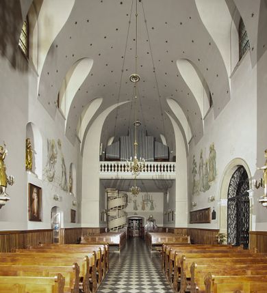 Zdjęcie nr 68: Kościół murowany, orientowany, jednonawowy, z transeptem, prezbiterium z obejściem i przybudówkami. Od zachodu kruchta, od północy kwadratowa kaplica, od południa kolejna przybudówka. 
Prezbiterium zamknięte półokrągło, z obejściem przeprutym do niego arkadami wspartymi na filarach. Ściany nawy i prezbiterium gładkie, przekryte sklepieniem kolebkowym z lunetami, w których mieszczą się okna. Transept i przecięcie naw sklepione krzyżowo. Na ścianach polichromia figuralna ze scenami z Nowego Testamentu, w partii sklepienia drobne, złote gwiazdki. Od zachodu chór zatopiony w występującym asymetrycznie murze, z tralkową balustradą. W prezbiterium siedem okien w kształcie stojącego prostokąta zamkniętego łukiem pełnym wypełnionych witrażami, w nawie sześć okien, w ramionach transeptu po jednym, czterodzielnym, wypełnionym witrażem, na wysokości chóru po dwa z każdej strony. Główne wejście od zachodu przez kruchtę. Fasada poprzedzona przedsionkiem o podziałach ramowych, z prostokątnym wejściem na osi, flankowanym parą pilastrów i prostokątnymi płycinami. Kondygnację wieńczy pełne belkowanie z wysuniętym gzymsem podtrzymującym daszek i trójkątny, schodkowy szczyt zakończony postumentami. Na centralnym krzyż, na sąsiadujących figury dzieci z rogami obfitości, a na zewnętrznych wazony płomieniste; szczyt ujmują postumenty z kulami. Fasada dwukondygnacyjna ze szczytem. Kondygnacja trójosiowa, rozdzielona pilastrami, o polach wypełnionych blendami w kształcie stojących prostokątów zamkniętych łukiem pełnym; szczyt trójkątny, z tarczą zegarową pośrodku. Budynek kościoła o wyraźnych podziałach na bryły składowe, ściany gładkie, przeprute oknami, z gzymsami pod krawędziami dachu. 
Nad nawą główną, na kalenicy, wieżyczka na sygnaturkę z latarnią i baniastym hełmem, druga na skrzyżowaniu naw, z latarnią i  hełmem zakończonym krzyżem. Dach nad nawą główną i przedsionkiem dwuspadowy, nad ramionami transeptu trójspadowym,nad prezbiterium zakończony wielobocznie, na przybudówkach dachy pulpitowe, dwuspadowe i wielospadowe. Dachy kryte dachówką ceramiczną, wieżyczki blachą. 
Najciekawszymi zabytkami kościoła są ołtarz główny z około 1700 roku z nastawą utworzoną z wici winnej latorośli, manierystyczny ołtarz boczny oraz siedemnastowieczna chrzcielnica z warsztatu Santi Gucciego. 
