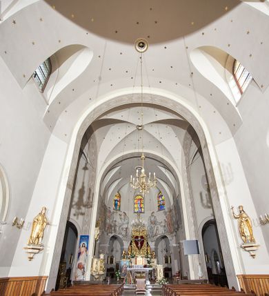 Zdjęcie nr 142: Kościół murowany, orientowany, jednonawowy, z transeptem, prezbiterium z obejściem i przybudówkami. Od zachodu kruchta, od północy kwadratowa kaplica, od południa kolejna przybudówka. 
Prezbiterium zamknięte półokrągło, z obejściem przeprutym do niego arkadami wspartymi na filarach. Ściany nawy i prezbiterium gładkie, przekryte sklepieniem kolebkowym z lunetami, w których mieszczą się okna. Transept i przecięcie naw sklepione krzyżowo. Na ścianach polichromia figuralna ze scenami z Nowego Testamentu, w partii sklepienia drobne, złote gwiazdki. Od zachodu chór zatopiony w występującym asymetrycznie murze, z tralkową balustradą. W prezbiterium siedem okien w kształcie stojącego prostokąta zamkniętego łukiem pełnym wypełnionych witrażami, w nawie sześć okien, w ramionach transeptu po jednym, czterodzielnym, wypełnionym witrażem, na wysokości chóru po dwa z każdej strony. Główne wejście od zachodu przez kruchtę. Fasada poprzedzona przedsionkiem o podziałach ramowych, z prostokątnym wejściem na osi, flankowanym parą pilastrów i prostokątnymi płycinami. Kondygnację wieńczy pełne belkowanie z wysuniętym gzymsem podtrzymującym daszek i trójkątny, schodkowy szczyt zakończony postumentami. Na centralnym krzyż, na sąsiadujących figury dzieci z rogami obfitości, a na zewnętrznych wazony płomieniste; szczyt ujmują postumenty z kulami. Fasada dwukondygnacyjna ze szczytem. Kondygnacja trójosiowa, rozdzielona pilastrami, o polach wypełnionych blendami w kształcie stojących prostokątów zamkniętych łukiem pełnym; szczyt trójkątny, z tarczą zegarową pośrodku. Budynek kościoła o wyraźnych podziałach na bryły składowe, ściany gładkie, przeprute oknami, z gzymsami pod krawędziami dachu. 
Nad nawą główną, na kalenicy, wieżyczka na sygnaturkę z latarnią i baniastym hełmem, druga na skrzyżowaniu naw, z latarnią i  hełmem zakończonym krzyżem. Dach nad nawą główną i przedsionkiem dwuspadowy, nad ramionami transeptu trójspadowym,nad prezbiterium zakończony wielobocznie, na przybudówkach dachy pulpitowe, dwuspadowe i wielospadowe. Dachy kryte dachówką ceramiczną, wieżyczki blachą. 
Najciekawszymi zabytkami kościoła są ołtarz główny z około 1700 roku z nastawą utworzoną z wici winnej latorośli, manierystyczny ołtarz boczny oraz siedemnastowieczna chrzcielnica z warsztatu Santi Gucciego. 
