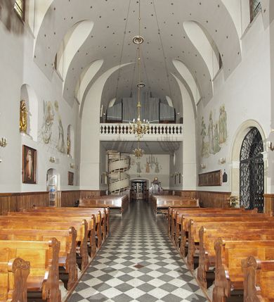 Zdjęcie nr 57: Kościół murowany, orientowany, jednonawowy, z transeptem, prezbiterium z obejściem i przybudówkami. Od zachodu kruchta, od północy kwadratowa kaplica, od południa kolejna przybudówka. 
Prezbiterium zamknięte półokrągło, z obejściem przeprutym do niego arkadami wspartymi na filarach. Ściany nawy i prezbiterium gładkie, przekryte sklepieniem kolebkowym z lunetami, w których mieszczą się okna. Transept i przecięcie naw sklepione krzyżowo. Na ścianach polichromia figuralna ze scenami z Nowego Testamentu, w partii sklepienia drobne, złote gwiazdki. Od zachodu chór zatopiony w występującym asymetrycznie murze, z tralkową balustradą. W prezbiterium siedem okien w kształcie stojącego prostokąta zamkniętego łukiem pełnym wypełnionych witrażami, w nawie sześć okien, w ramionach transeptu po jednym, czterodzielnym, wypełnionym witrażem, na wysokości chóru po dwa z każdej strony. Główne wejście od zachodu przez kruchtę. Fasada poprzedzona przedsionkiem o podziałach ramowych, z prostokątnym wejściem na osi, flankowanym parą pilastrów i prostokątnymi płycinami. Kondygnację wieńczy pełne belkowanie z wysuniętym gzymsem podtrzymującym daszek i trójkątny, schodkowy szczyt zakończony postumentami. Na centralnym krzyż, na sąsiadujących figury dzieci z rogami obfitości, a na zewnętrznych wazony płomieniste; szczyt ujmują postumenty z kulami. Fasada dwukondygnacyjna ze szczytem. Kondygnacja trójosiowa, rozdzielona pilastrami, o polach wypełnionych blendami w kształcie stojących prostokątów zamkniętych łukiem pełnym; szczyt trójkątny, z tarczą zegarową pośrodku. Budynek kościoła o wyraźnych podziałach na bryły składowe, ściany gładkie, przeprute oknami, z gzymsami pod krawędziami dachu. 
Nad nawą główną, na kalenicy, wieżyczka na sygnaturkę z latarnią i baniastym hełmem, druga na skrzyżowaniu naw, z latarnią i  hełmem zakończonym krzyżem. Dach nad nawą główną i przedsionkiem dwuspadowy, nad ramionami transeptu trójspadowym,nad prezbiterium zakończony wielobocznie, na przybudówkach dachy pulpitowe, dwuspadowe i wielospadowe. Dachy kryte dachówką ceramiczną, wieżyczki blachą. 
Najciekawszymi zabytkami kościoła są ołtarz główny z około 1700 roku z nastawą utworzoną z wici winnej latorośli, manierystyczny ołtarz boczny oraz siedemnastowieczna chrzcielnica z warsztatu Santi Gucciego. 
