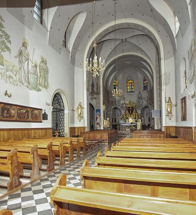 Zdjęcie nr 101: Kościół murowany, orientowany, jednonawowy, z transeptem, prezbiterium z obejściem i przybudówkami. Od zachodu kruchta, od północy kwadratowa kaplica, od południa kolejna przybudówka. 
Prezbiterium zamknięte półokrągło, z obejściem przeprutym do niego arkadami wspartymi na filarach. Ściany nawy i prezbiterium gładkie, przekryte sklepieniem kolebkowym z lunetami, w których mieszczą się okna. Transept i przecięcie naw sklepione krzyżowo. Na ścianach polichromia figuralna ze scenami z Nowego Testamentu, w partii sklepienia drobne, złote gwiazdki. Od zachodu chór zatopiony w występującym asymetrycznie murze, z tralkową balustradą. W prezbiterium siedem okien w kształcie stojącego prostokąta zamkniętego łukiem pełnym wypełnionych witrażami, w nawie sześć okien, w ramionach transeptu po jednym, czterodzielnym, wypełnionym witrażem, na wysokości chóru po dwa z każdej strony. Główne wejście od zachodu przez kruchtę. Fasada poprzedzona przedsionkiem o podziałach ramowych, z prostokątnym wejściem na osi, flankowanym parą pilastrów i prostokątnymi płycinami. Kondygnację wieńczy pełne belkowanie z wysuniętym gzymsem podtrzymującym daszek i trójkątny, schodkowy szczyt zakończony postumentami. Na centralnym krzyż, na sąsiadujących figury dzieci z rogami obfitości, a na zewnętrznych wazony płomieniste; szczyt ujmują postumenty z kulami. Fasada dwukondygnacyjna ze szczytem. Kondygnacja trójosiowa, rozdzielona pilastrami, o polach wypełnionych blendami w kształcie stojących prostokątów zamkniętych łukiem pełnym; szczyt trójkątny, z tarczą zegarową pośrodku. Budynek kościoła o wyraźnych podziałach na bryły składowe, ściany gładkie, przeprute oknami, z gzymsami pod krawędziami dachu. 
Nad nawą główną, na kalenicy, wieżyczka na sygnaturkę z latarnią i baniastym hełmem, druga na skrzyżowaniu naw, z latarnią i  hełmem zakończonym krzyżem. Dach nad nawą główną i przedsionkiem dwuspadowy, nad ramionami transeptu trójspadowym,nad prezbiterium zakończony wielobocznie, na przybudówkach dachy pulpitowe, dwuspadowe i wielospadowe. Dachy kryte dachówką ceramiczną, wieżyczki blachą. 
Najciekawszymi zabytkami kościoła są ołtarz główny z około 1700 roku z nastawą utworzoną z wici winnej latorośli, manierystyczny ołtarz boczny oraz siedemnastowieczna chrzcielnica z warsztatu Santi Gucciego. 
