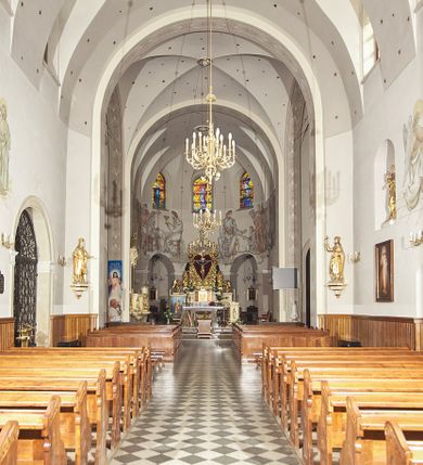 Zdjęcie nr 46: Kościół murowany, orientowany, jednonawowy, z transeptem, prezbiterium z obejściem i przybudówkami. Od zachodu kruchta, od północy kwadratowa kaplica, od południa kolejna przybudówka. 
Prezbiterium zamknięte półokrągło, z obejściem przeprutym do niego arkadami wspartymi na filarach. Ściany nawy i prezbiterium gładkie, przekryte sklepieniem kolebkowym z lunetami, w których mieszczą się okna. Transept i przecięcie naw sklepione krzyżowo. Na ścianach polichromia figuralna ze scenami z Nowego Testamentu, w partii sklepienia drobne, złote gwiazdki. Od zachodu chór zatopiony w występującym asymetrycznie murze, z tralkową balustradą. W prezbiterium siedem okien w kształcie stojącego prostokąta zamkniętego łukiem pełnym wypełnionych witrażami, w nawie sześć okien, w ramionach transeptu po jednym, czterodzielnym, wypełnionym witrażem, na wysokości chóru po dwa z każdej strony. Główne wejście od zachodu przez kruchtę. Fasada poprzedzona przedsionkiem o podziałach ramowych, z prostokątnym wejściem na osi, flankowanym parą pilastrów i prostokątnymi płycinami. Kondygnację wieńczy pełne belkowanie z wysuniętym gzymsem podtrzymującym daszek i trójkątny, schodkowy szczyt zakończony postumentami. Na centralnym krzyż, na sąsiadujących figury dzieci z rogami obfitości, a na zewnętrznych wazony płomieniste; szczyt ujmują postumenty z kulami. Fasada dwukondygnacyjna ze szczytem. Kondygnacja trójosiowa, rozdzielona pilastrami, o polach wypełnionych blendami w kształcie stojących prostokątów zamkniętych łukiem pełnym; szczyt trójkątny, z tarczą zegarową pośrodku. Budynek kościoła o wyraźnych podziałach na bryły składowe, ściany gładkie, przeprute oknami, z gzymsami pod krawędziami dachu. 
Nad nawą główną, na kalenicy, wieżyczka na sygnaturkę z latarnią i baniastym hełmem, druga na skrzyżowaniu naw, z latarnią i  hełmem zakończonym krzyżem. Dach nad nawą główną i przedsionkiem dwuspadowy, nad ramionami transeptu trójspadowym,nad prezbiterium zakończony wielobocznie, na przybudówkach dachy pulpitowe, dwuspadowe i wielospadowe. Dachy kryte dachówką ceramiczną, wieżyczki blachą. 
Najciekawszymi zabytkami kościoła są ołtarz główny z około 1700 roku z nastawą utworzoną z wici winnej latorośli, manierystyczny ołtarz boczny oraz siedemnastowieczna chrzcielnica z warsztatu Santi Gucciego. 
