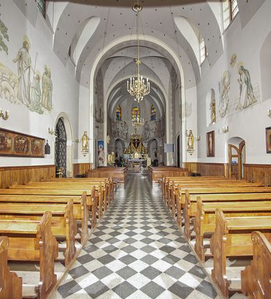 Zdjęcie nr 36: Kościół murowany, orientowany, jednonawowy, z transeptem, prezbiterium z obejściem i przybudówkami. Od zachodu kruchta, od północy kwadratowa kaplica, od południa kolejna przybudówka. 
Prezbiterium zamknięte półokrągło, z obejściem przeprutym do niego arkadami wspartymi na filarach. Ściany nawy i prezbiterium gładkie, przekryte sklepieniem kolebkowym z lunetami, w których mieszczą się okna. Transept i przecięcie naw sklepione krzyżowo. Na ścianach polichromia figuralna ze scenami z Nowego Testamentu, w partii sklepienia drobne, złote gwiazdki. Od zachodu chór zatopiony w występującym asymetrycznie murze, z tralkową balustradą. W prezbiterium siedem okien w kształcie stojącego prostokąta zamkniętego łukiem pełnym wypełnionych witrażami, w nawie sześć okien, w ramionach transeptu po jednym, czterodzielnym, wypełnionym witrażem, na wysokości chóru po dwa z każdej strony. Główne wejście od zachodu przez kruchtę. Fasada poprzedzona przedsionkiem o podziałach ramowych, z prostokątnym wejściem na osi, flankowanym parą pilastrów i prostokątnymi płycinami. Kondygnację wieńczy pełne belkowanie z wysuniętym gzymsem podtrzymującym daszek i trójkątny, schodkowy szczyt zakończony postumentami. Na centralnym krzyż, na sąsiadujących figury dzieci z rogami obfitości, a na zewnętrznych wazony płomieniste; szczyt ujmują postumenty z kulami. Fasada dwukondygnacyjna ze szczytem. Kondygnacja trójosiowa, rozdzielona pilastrami, o polach wypełnionych blendami w kształcie stojących prostokątów zamkniętych łukiem pełnym; szczyt trójkątny, z tarczą zegarową pośrodku. Budynek kościoła o wyraźnych podziałach na bryły składowe, ściany gładkie, przeprute oknami, z gzymsami pod krawędziami dachu. 
Nad nawą główną, na kalenicy, wieżyczka na sygnaturkę z latarnią i baniastym hełmem, druga na skrzyżowaniu naw, z latarnią i  hełmem zakończonym krzyżem. Dach nad nawą główną i przedsionkiem dwuspadowy, nad ramionami transeptu trójspadowym,nad prezbiterium zakończony wielobocznie, na przybudówkach dachy pulpitowe, dwuspadowe i wielospadowe. Dachy kryte dachówką ceramiczną, wieżyczki blachą. 
Najciekawszymi zabytkami kościoła są ołtarz główny z około 1700 roku z nastawą utworzoną z wici winnej latorośli, manierystyczny ołtarz boczny oraz siedemnastowieczna chrzcielnica z warsztatu Santi Gucciego. 
