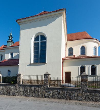 Zdjęcie nr 12: Kościół murowany, orientowany, jednonawowy, z transeptem, prezbiterium z obejściem i przybudówkami. Od zachodu kruchta, od północy kwadratowa kaplica, od południa kolejna przybudówka. 
Prezbiterium zamknięte półokrągło, z obejściem przeprutym do niego arkadami wspartymi na filarach. Ściany nawy i prezbiterium gładkie, przekryte sklepieniem kolebkowym z lunetami, w których mieszczą się okna. Transept i przecięcie naw sklepione krzyżowo. Na ścianach polichromia figuralna ze scenami z Nowego Testamentu, w partii sklepienia drobne, złote gwiazdki. Od zachodu chór zatopiony w występującym asymetrycznie murze, z tralkową balustradą. W prezbiterium siedem okien w kształcie stojącego prostokąta zamkniętego łukiem pełnym wypełnionych witrażami, w nawie sześć okien, w ramionach transeptu po jednym, czterodzielnym, wypełnionym witrażem, na wysokości chóru po dwa z każdej strony. Główne wejście od zachodu przez kruchtę. Fasada poprzedzona przedsionkiem o podziałach ramowych, z prostokątnym wejściem na osi, flankowanym parą pilastrów i prostokątnymi płycinami. Kondygnację wieńczy pełne belkowanie z wysuniętym gzymsem podtrzymującym daszek i trójkątny, schodkowy szczyt zakończony postumentami. Na centralnym krzyż, na sąsiadujących figury dzieci z rogami obfitości, a na zewnętrznych wazony płomieniste; szczyt ujmują postumenty z kulami. Fasada dwukondygnacyjna ze szczytem. Kondygnacja trójosiowa, rozdzielona pilastrami, o polach wypełnionych blendami w kształcie stojących prostokątów zamkniętych łukiem pełnym; szczyt trójkątny, z tarczą zegarową pośrodku. Budynek kościoła o wyraźnych podziałach na bryły składowe, ściany gładkie, przeprute oknami, z gzymsami pod krawędziami dachu. 
Nad nawą główną, na kalenicy, wieżyczka na sygnaturkę z latarnią i baniastym hełmem, druga na skrzyżowaniu naw, z latarnią i  hełmem zakończonym krzyżem. Dach nad nawą główną i przedsionkiem dwuspadowy, nad ramionami transeptu trójspadowym,nad prezbiterium zakończony wielobocznie, na przybudówkach dachy pulpitowe, dwuspadowe i wielospadowe. Dachy kryte dachówką ceramiczną, wieżyczki blachą. 
Najciekawszymi zabytkami kościoła są ołtarz główny z około 1700 roku z nastawą utworzoną z wici winnej latorośli, manierystyczny ołtarz boczny oraz siedemnastowieczna chrzcielnica z warsztatu Santi Gucciego. 
