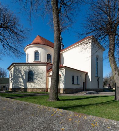 Zdjęcie nr 11: Kościół murowany, orientowany, jednonawowy, z transeptem, prezbiterium z obejściem i przybudówkami. Od zachodu kruchta, od północy kwadratowa kaplica, od południa kolejna przybudówka. 
Prezbiterium zamknięte półokrągło, z obejściem przeprutym do niego arkadami wspartymi na filarach. Ściany nawy i prezbiterium gładkie, przekryte sklepieniem kolebkowym z lunetami, w których mieszczą się okna. Transept i przecięcie naw sklepione krzyżowo. Na ścianach polichromia figuralna ze scenami z Nowego Testamentu, w partii sklepienia drobne, złote gwiazdki. Od zachodu chór zatopiony w występującym asymetrycznie murze, z tralkową balustradą. W prezbiterium siedem okien w kształcie stojącego prostokąta zamkniętego łukiem pełnym wypełnionych witrażami, w nawie sześć okien, w ramionach transeptu po jednym, czterodzielnym, wypełnionym witrażem, na wysokości chóru po dwa z każdej strony. Główne wejście od zachodu przez kruchtę. Fasada poprzedzona przedsionkiem o podziałach ramowych, z prostokątnym wejściem na osi, flankowanym parą pilastrów i prostokątnymi płycinami. Kondygnację wieńczy pełne belkowanie z wysuniętym gzymsem podtrzymującym daszek i trójkątny, schodkowy szczyt zakończony postumentami. Na centralnym krzyż, na sąsiadujących figury dzieci z rogami obfitości, a na zewnętrznych wazony płomieniste; szczyt ujmują postumenty z kulami. Fasada dwukondygnacyjna ze szczytem. Kondygnacja trójosiowa, rozdzielona pilastrami, o polach wypełnionych blendami w kształcie stojących prostokątów zamkniętych łukiem pełnym; szczyt trójkątny, z tarczą zegarową pośrodku. Budynek kościoła o wyraźnych podziałach na bryły składowe, ściany gładkie, przeprute oknami, z gzymsami pod krawędziami dachu. 
Nad nawą główną, na kalenicy, wieżyczka na sygnaturkę z latarnią i baniastym hełmem, druga na skrzyżowaniu naw, z latarnią i  hełmem zakończonym krzyżem. Dach nad nawą główną i przedsionkiem dwuspadowy, nad ramionami transeptu trójspadowym,nad prezbiterium zakończony wielobocznie, na przybudówkach dachy pulpitowe, dwuspadowe i wielospadowe. Dachy kryte dachówką ceramiczną, wieżyczki blachą. 
Najciekawszymi zabytkami kościoła są ołtarz główny z około 1700 roku z nastawą utworzoną z wici winnej latorośli, manierystyczny ołtarz boczny oraz siedemnastowieczna chrzcielnica z warsztatu Santi Gucciego. 
