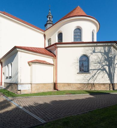 Zdjęcie nr 16: Kościół murowany, orientowany, jednonawowy, z transeptem, prezbiterium z obejściem i przybudówkami. Od zachodu kruchta, od północy kwadratowa kaplica, od południa kolejna przybudówka. 
Prezbiterium zamknięte półokrągło, z obejściem przeprutym do niego arkadami wspartymi na filarach. Ściany nawy i prezbiterium gładkie, przekryte sklepieniem kolebkowym z lunetami, w których mieszczą się okna. Transept i przecięcie naw sklepione krzyżowo. Na ścianach polichromia figuralna ze scenami z Nowego Testamentu, w partii sklepienia drobne, złote gwiazdki. Od zachodu chór zatopiony w występującym asymetrycznie murze, z tralkową balustradą. W prezbiterium siedem okien w kształcie stojącego prostokąta zamkniętego łukiem pełnym wypełnionych witrażami, w nawie sześć okien, w ramionach transeptu po jednym, czterodzielnym, wypełnionym witrażem, na wysokości chóru po dwa z każdej strony. Główne wejście od zachodu przez kruchtę. Fasada poprzedzona przedsionkiem o podziałach ramowych, z prostokątnym wejściem na osi, flankowanym parą pilastrów i prostokątnymi płycinami. Kondygnację wieńczy pełne belkowanie z wysuniętym gzymsem podtrzymującym daszek i trójkątny, schodkowy szczyt zakończony postumentami. Na centralnym krzyż, na sąsiadujących figury dzieci z rogami obfitości, a na zewnętrznych wazony płomieniste; szczyt ujmują postumenty z kulami. Fasada dwukondygnacyjna ze szczytem. Kondygnacja trójosiowa, rozdzielona pilastrami, o polach wypełnionych blendami w kształcie stojących prostokątów zamkniętych łukiem pełnym; szczyt trójkątny, z tarczą zegarową pośrodku. Budynek kościoła o wyraźnych podziałach na bryły składowe, ściany gładkie, przeprute oknami, z gzymsami pod krawędziami dachu. 
Nad nawą główną, na kalenicy, wieżyczka na sygnaturkę z latarnią i baniastym hełmem, druga na skrzyżowaniu naw, z latarnią i  hełmem zakończonym krzyżem. Dach nad nawą główną i przedsionkiem dwuspadowy, nad ramionami transeptu trójspadowym,nad prezbiterium zakończony wielobocznie, na przybudówkach dachy pulpitowe, dwuspadowe i wielospadowe. Dachy kryte dachówką ceramiczną, wieżyczki blachą. 
Najciekawszymi zabytkami kościoła są ołtarz główny z około 1700 roku z nastawą utworzoną z wici winnej latorośli, manierystyczny ołtarz boczny oraz siedemnastowieczna chrzcielnica z warsztatu Santi Gucciego. 
